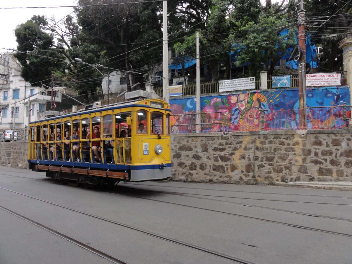 Tramway historique jaune plein de passagers passant devant un mur de graffiti coloré en ville.