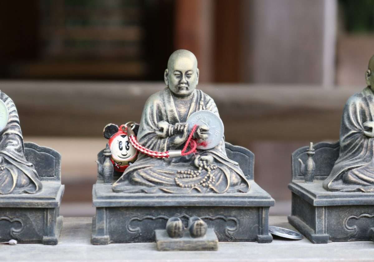 Statuette de moine bouddhiste en méditation avec un petit porte-bonheur de personnage de dessin animé à ses côtés.