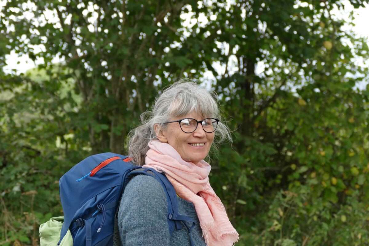 Bozena Le Talludec, souriante avec des lunettes, prête pour une randonnée, symbolise l'esprit d'aventure à travers ses récits de voyage.