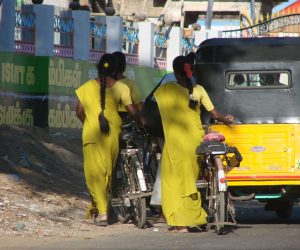 Deux personnes en vêtements traditionnels jaunes à l'arrière d'un rickshaw motorisé sur une route de ville.