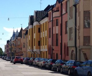 Rue ensoleillée bordée de maisons colorées aux façades vives et voitures garées dans une ville européenne.